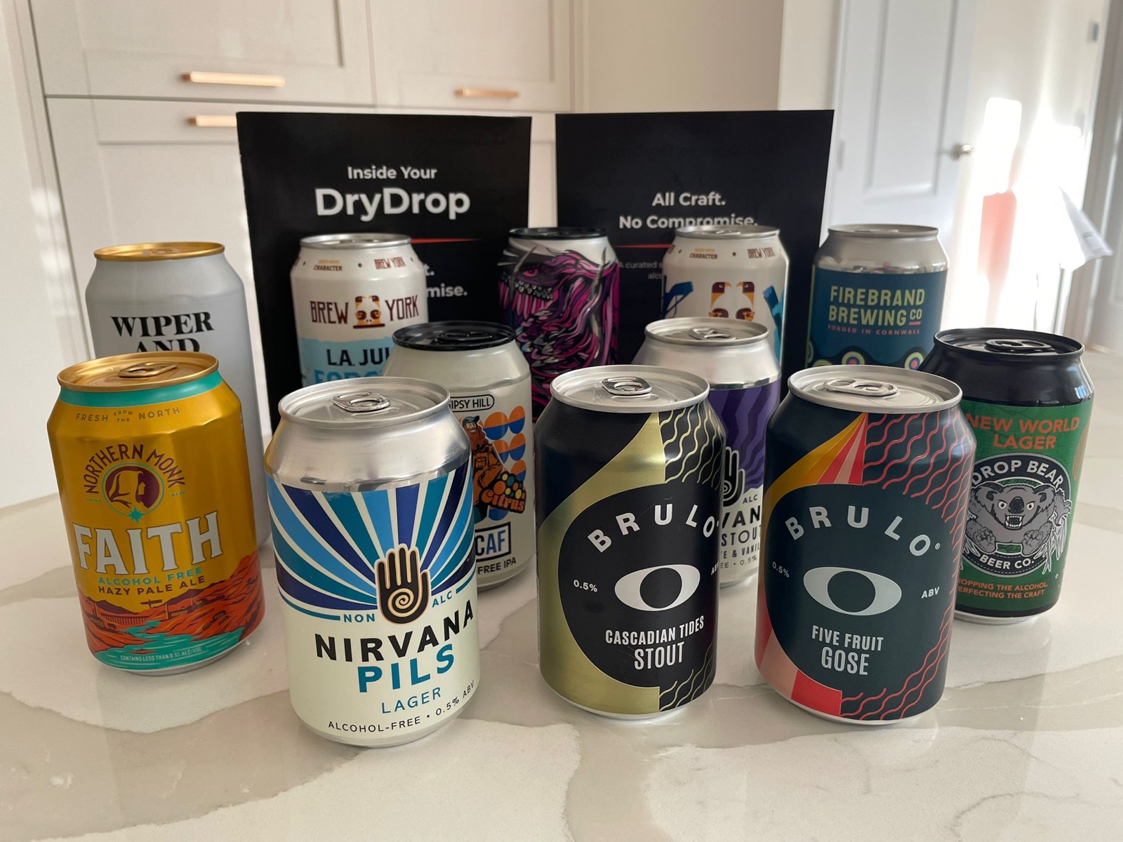 DryDrop Founders Box contents — 11 alcohol-free craft beer cans including Northern Monk Faith, Nirvana Pils, Brulo Cascadian Tides Stout, Brulo Five Fruit Gose, Drop Bear New World Lager, Wiper and True, Brew York, Firebrand Brewing Co. and Gipsy Hill