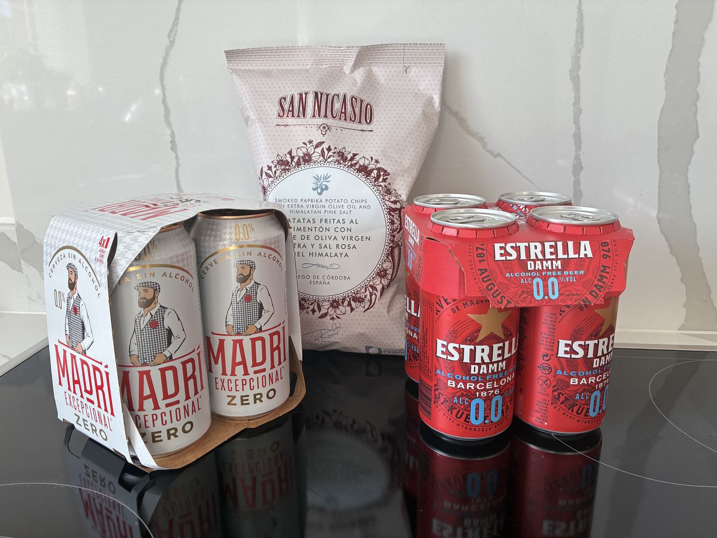 Madri Excepcional Zero and Estrella Damm 0.0 four-packs with San Nicasio paprika crisps on a kitchen counter