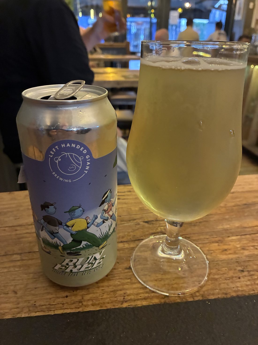A can of Left Handed Giant Run Free alcohol-free IPA poured into a glass on a pub table