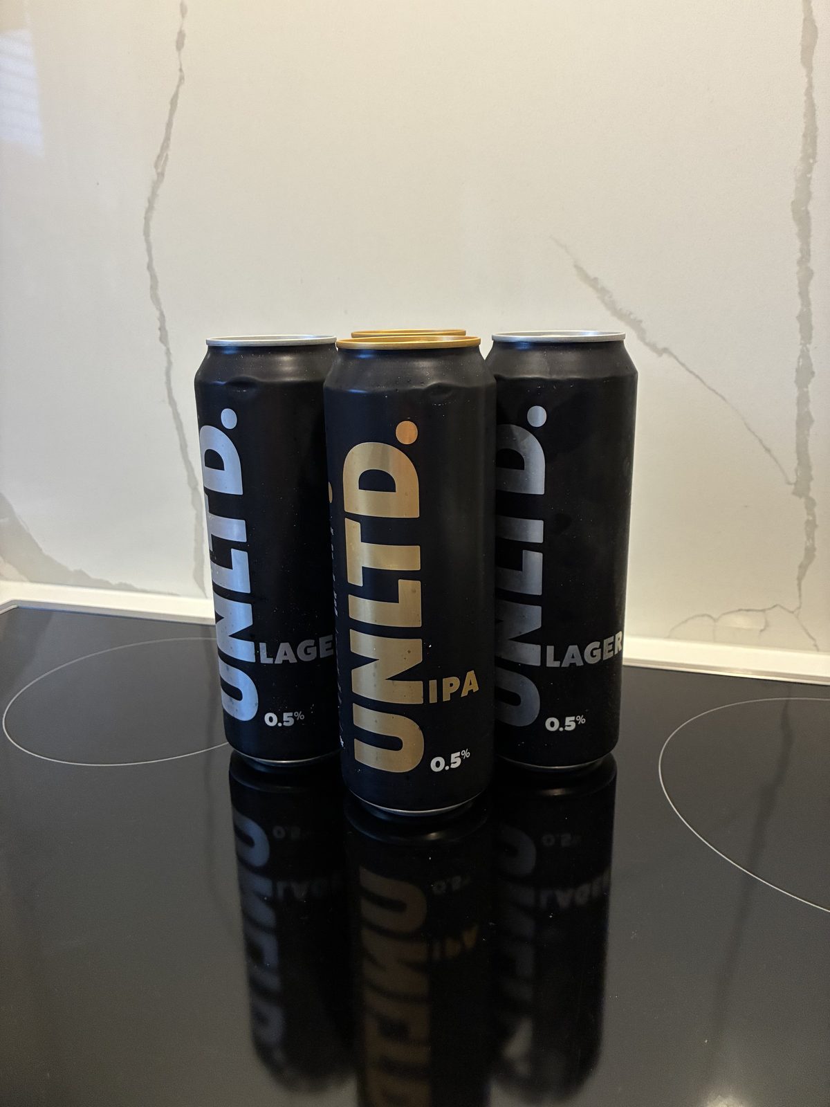 Three UNLTD alcohol-free beer cans &mdash; two Lager and one IPA, all 0.5% ABV